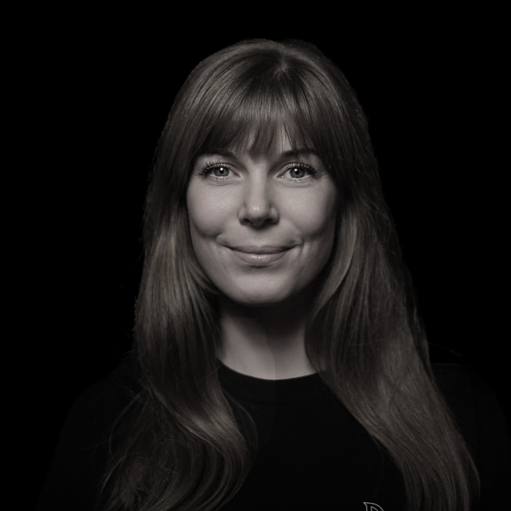 dunkles schwarz weiß Foto einer Frau die in einem Portraitformat lächelnd in die Kamera schaut.