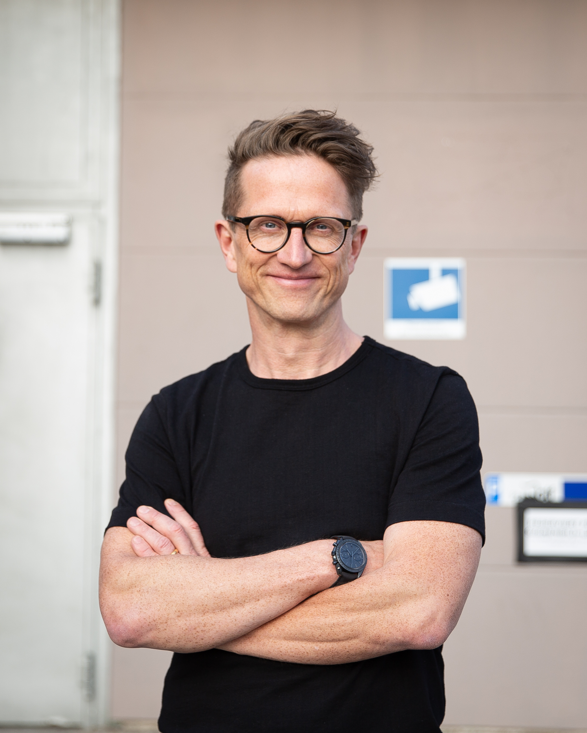 lächelnder Mann mit braunen Haaren und Brille und schwarzem Shirt, der lächelnd in die Kamera schaut
